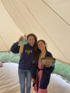 This image shows Charlotte (CEO of LOOK) & Nazan standing together, smiling at the camera. Nazan has a Tibetan bowl in her hand, and Charlotte has a Koshi Chime in her hand. They are stood in a yurt. 