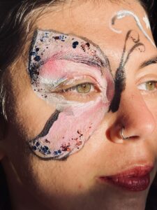 This image shows a close up of Nazan's face, face painted! There are patterned stars and swirls, and a huge butterfly around her eye. 