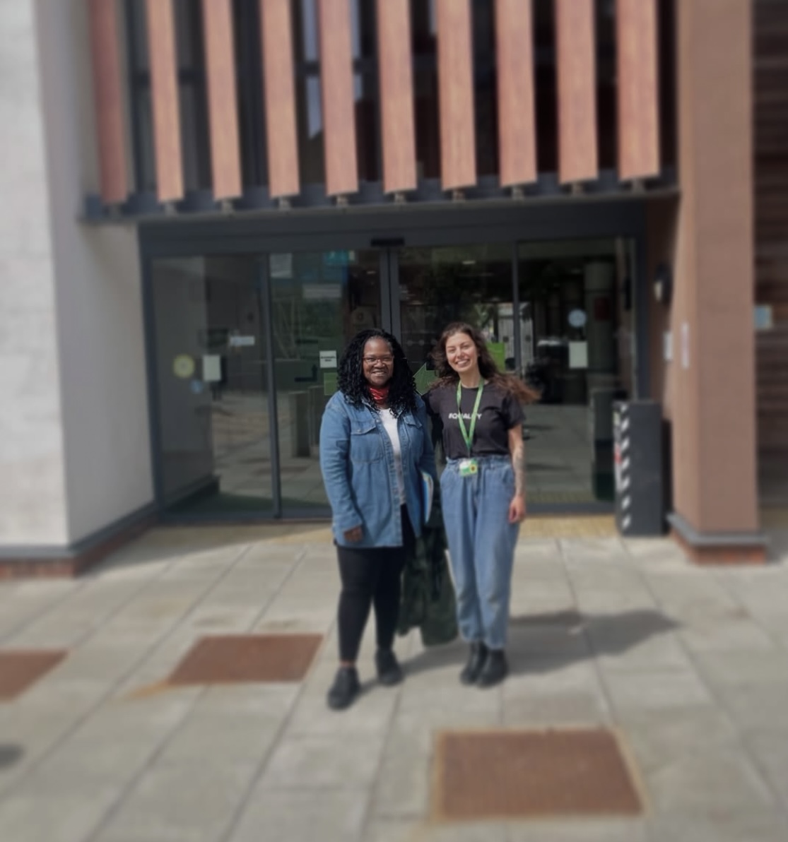 This image shows Nazan and Barbara (Founder of Breaking Down Barriers) standing in front of a council building after Nazan's first (of many) Equality, Diversity, & Inclusion speeches. They are both smiling at the camera, and the background is blurred. It is a sunny day!